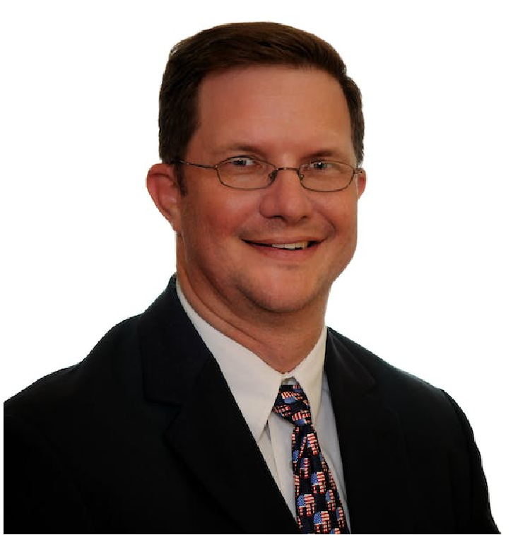 Smiling man in a black suit and patterned tie, wearing glasses, against a white background.